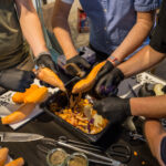 Nahaufnahme von Händen die zusammen bei einem Grillabend Süßkartoffeln schälen